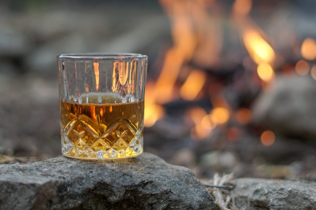 Learn whiskey terms with a vintage crystal glass of bourbon by an outdoor campfire