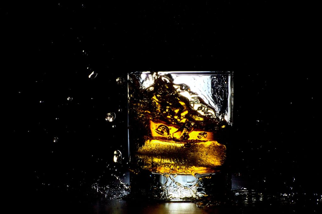 Photo shows tumbler of whiskey on ice, against a dark background. Credit to Mathew Schwartz via Unsplash
