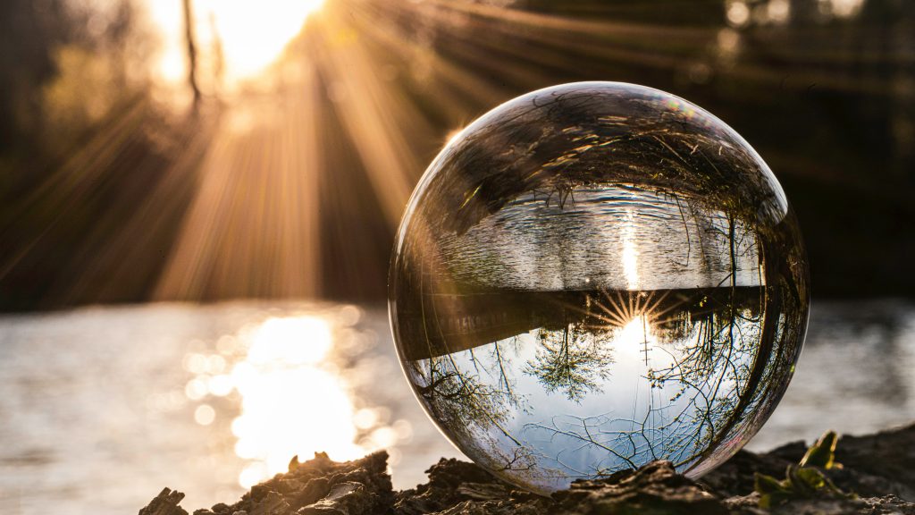 Picture of a crystal ball by a river with sun shining through. Credit Brad Switzer via Unsplash
