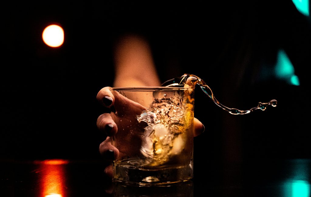 Picture shows hand holding whiskey glass, smashing onto a bar. whiskey is spilling out of glass.